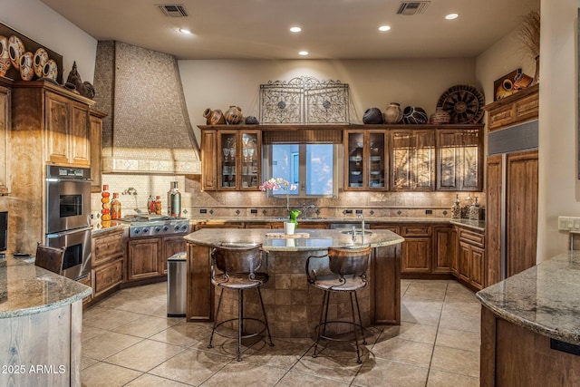 kitchen featuring stainless steel appliances, a center island with sink, tasteful backsplash, light stone counters, and a breakfast bar