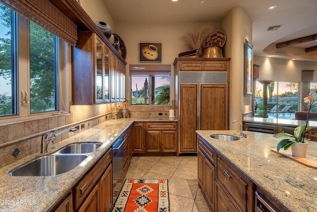 kitchen with a sink, paneled built in fridge, brown cabinets, recessed lighting, and light tile patterned floors