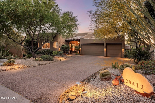 adobe home with stucco siding, driveway, a garage, and a tiled roof