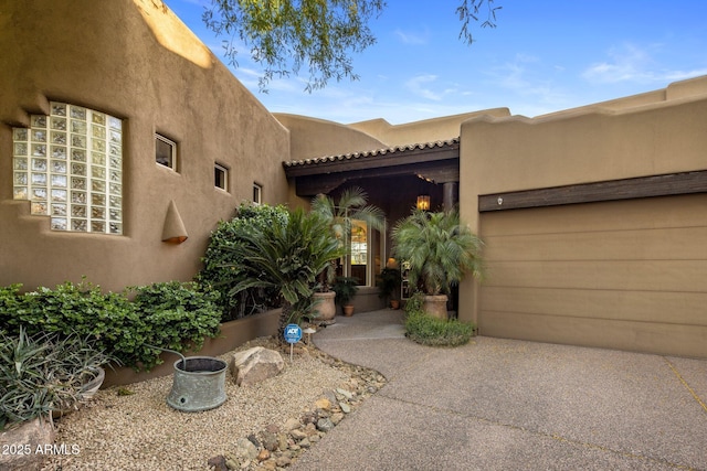 property entrance with stucco siding, a garage, and driveway