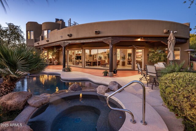 rear view of house featuring a patio area, a pool with connected hot tub, and a balcony