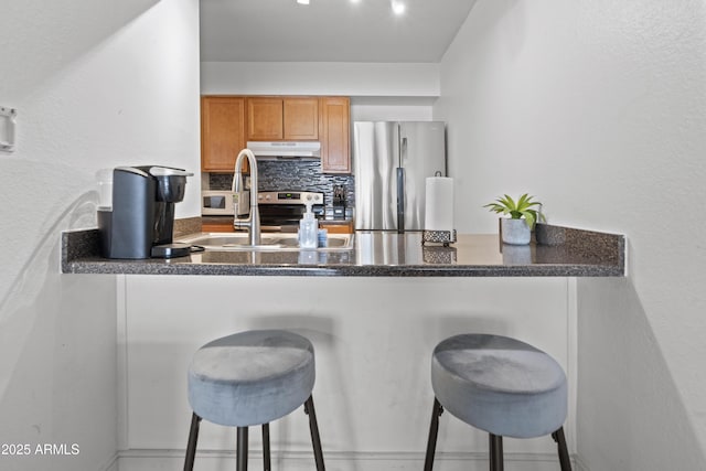 kitchen with a kitchen bar, sink, decorative backsplash, and stainless steel refrigerator