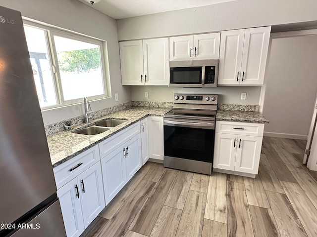 kitchen with white cabinets, light stone countertops, stainless steel appliances, light wood-type flooring, and sink