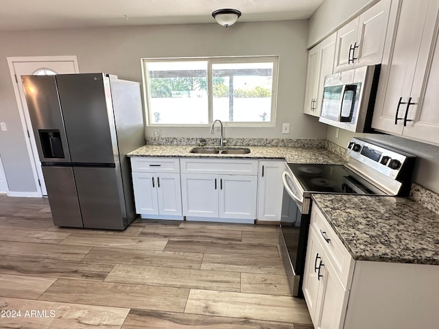 kitchen with appliances with stainless steel finishes, light hardwood / wood-style floors, light stone counters, white cabinets, and sink