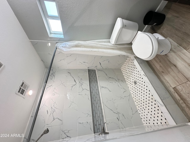 bathroom featuring a textured ceiling, toilet, and tiled shower