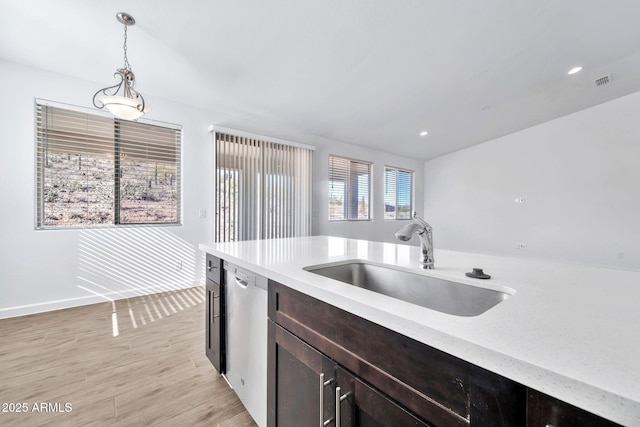 kitchen featuring sink, light stone counters, stainless steel dishwasher, decorative light fixtures, and light wood-type flooring