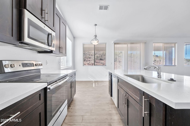 kitchen with pendant lighting, dark brown cabinetry, sink, and appliances with stainless steel finishes