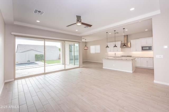 unfurnished living room with a tray ceiling, ceiling fan, sink, and light hardwood / wood-style floors