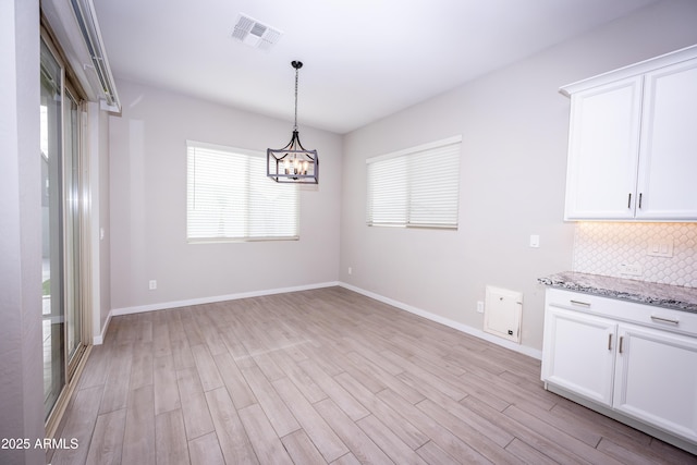 unfurnished dining area featuring light wood-type flooring and an inviting chandelier