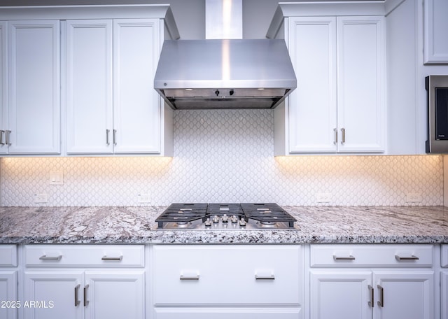 kitchen with white cabinets, stainless steel gas stovetop, wall chimney range hood, and backsplash