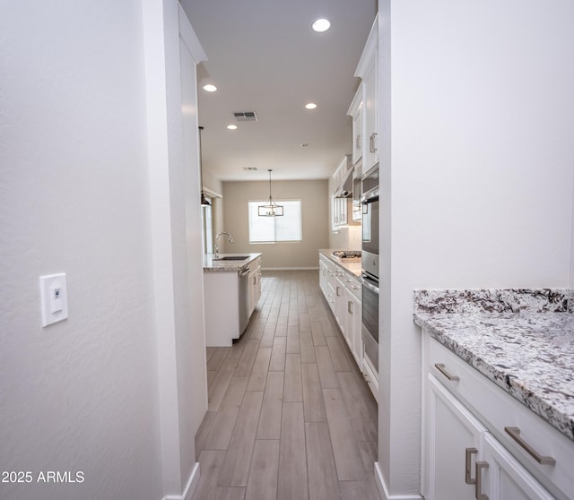 kitchen with light stone countertops, stainless steel appliances, sink, decorative light fixtures, and white cabinetry