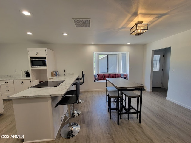 kitchen with white cabinetry, black electric stovetop, stainless steel microwave, and light wood-type flooring