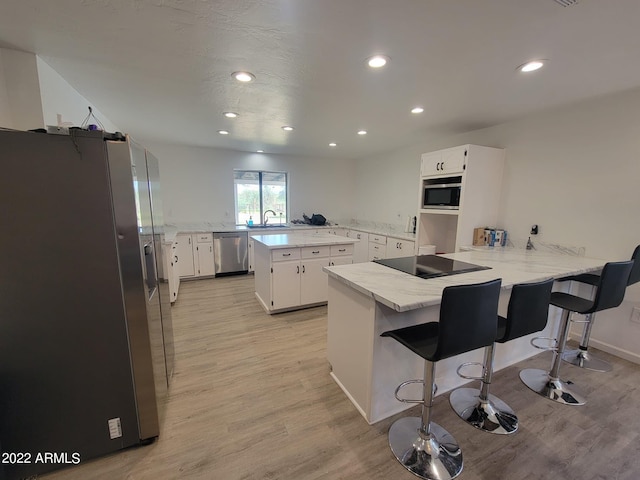 kitchen featuring a kitchen breakfast bar, kitchen peninsula, white cabinets, and appliances with stainless steel finishes