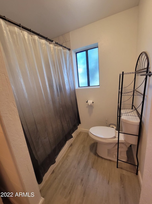 bathroom featuring wood-type flooring, toilet, and curtained shower