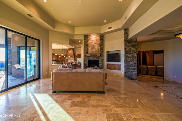 living room featuring a tray ceiling, a stone fireplace, and a high ceiling