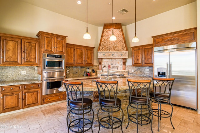 kitchen featuring a kitchen breakfast bar, a high ceiling, stainless steel built in refrigerator, light stone countertops, and decorative light fixtures