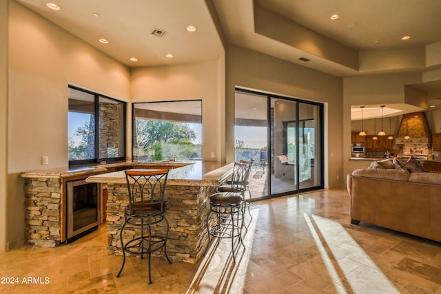 bar with premium range hood, a high ceiling, wine cooler, light stone countertops, and decorative light fixtures