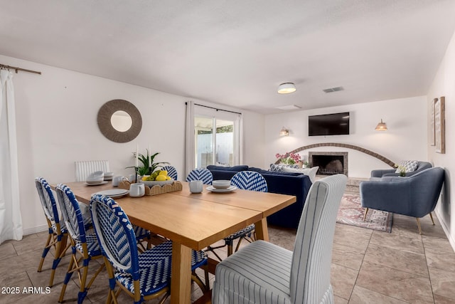 dining area featuring a fireplace with raised hearth, visible vents, and baseboards