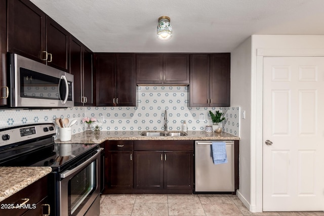 kitchen featuring stainless steel appliances, tasteful backsplash, a sink, dark brown cabinets, and light stone countertops