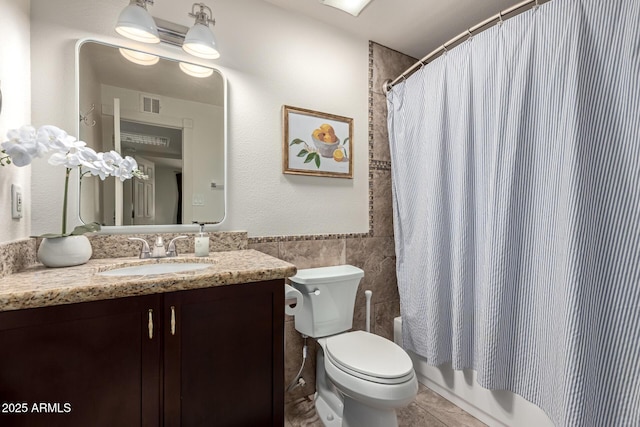 bathroom featuring tile patterned flooring, toilet, shower / tub combo, vanity, and tile walls