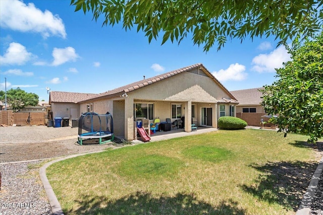 rear view of property featuring fence, a patio, a trampoline, stucco siding, and a yard