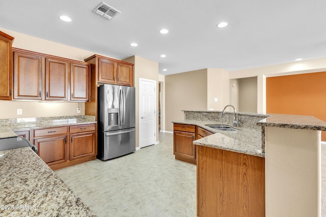 kitchen featuring stainless steel fridge, visible vents, brown cabinetry, and a sink