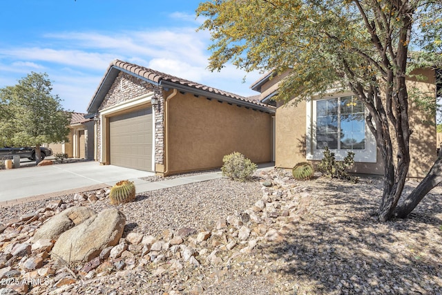 view of front of house with a tiled roof, concrete driveway, an attached garage, and stucco siding