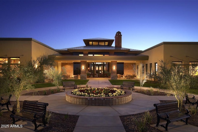 back of property at dusk featuring metal roof, a standing seam roof, a chimney, and stucco siding