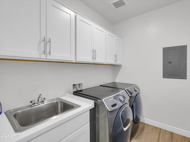 washroom featuring sink, electric panel, cabinets, wood-type flooring, and separate washer and dryer