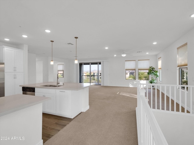 kitchen with sink, white cabinetry, hanging light fixtures, stainless steel dishwasher, and an island with sink