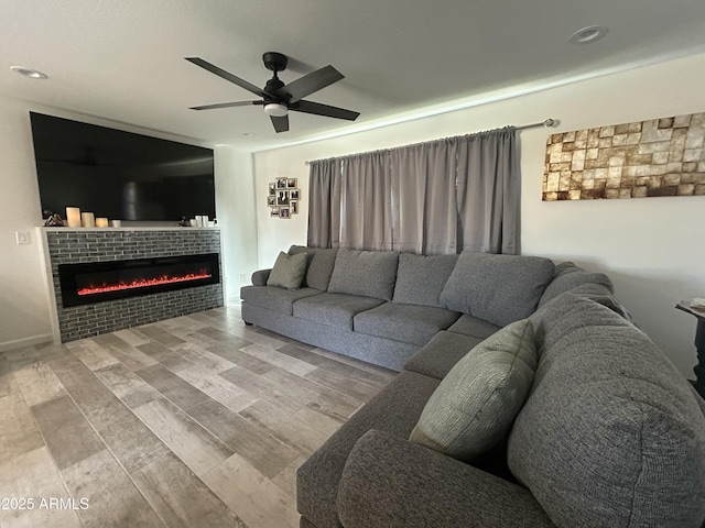 living room with a tiled fireplace, ceiling fan, and light wood-type flooring