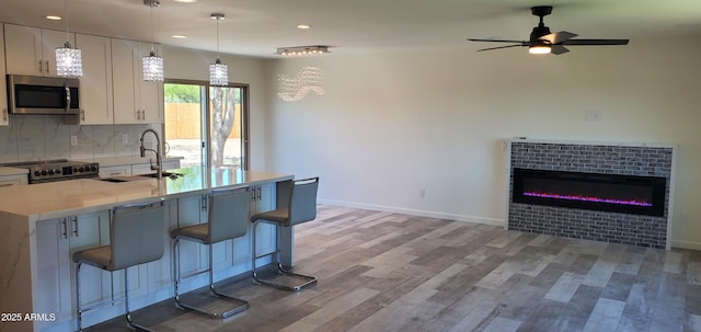 kitchen with white cabinetry, a kitchen bar, hanging light fixtures, stainless steel appliances, and a center island with sink