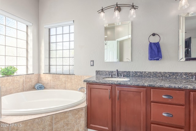 bathroom featuring tiled tub, vanity, and a healthy amount of sunlight