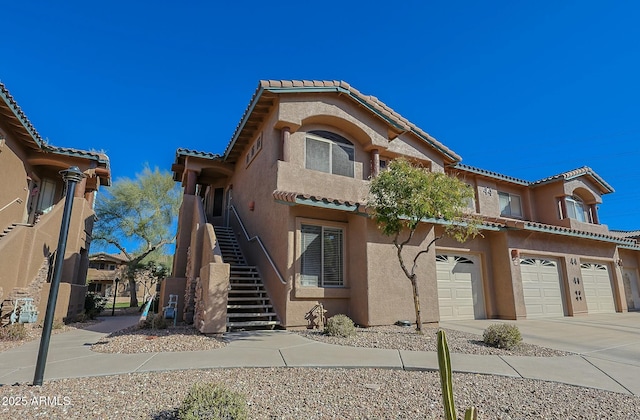 view of front facade with an attached garage, stairs, driveway, a tiled roof, and stucco siding