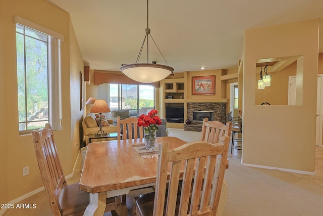 dining room with light carpet, a stone fireplace, and baseboards