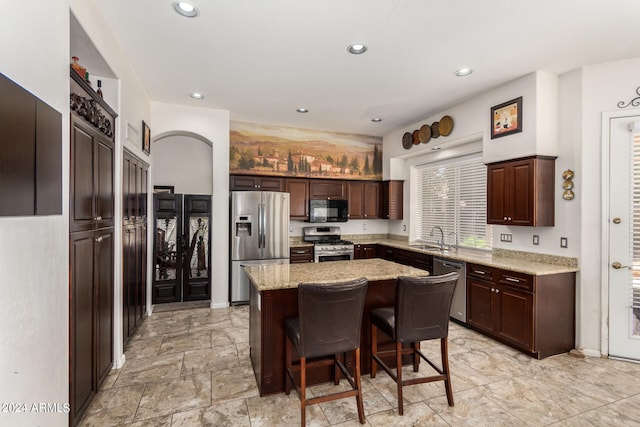 kitchen with appliances with stainless steel finishes, light stone counters, sink, a kitchen island, and a breakfast bar