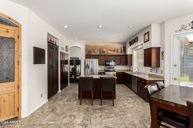 kitchen with a kitchen island, light stone countertops, dark brown cabinets, appliances with stainless steel finishes, and sink