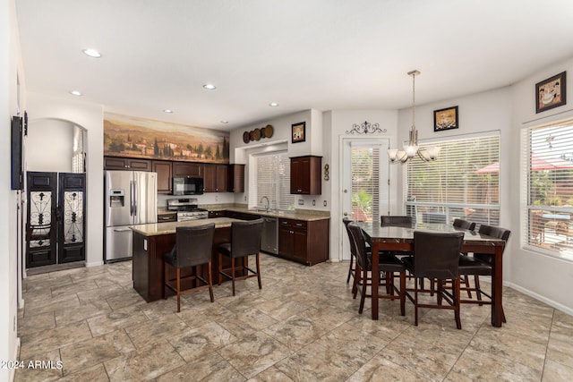 kitchen with dark brown cabinets, a chandelier, stainless steel appliances, decorative light fixtures, and a kitchen island