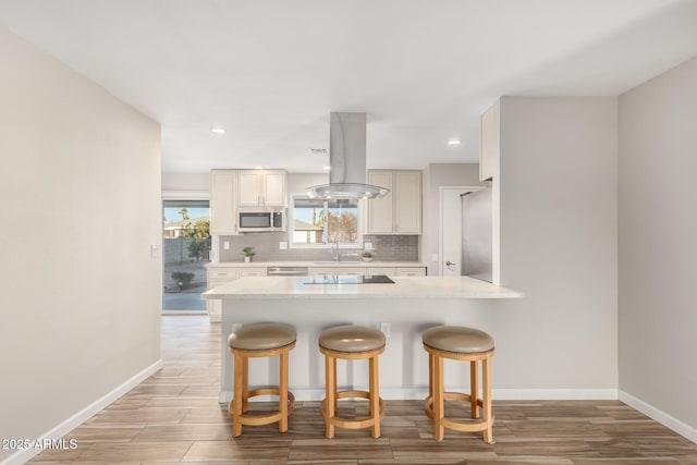 kitchen featuring stainless steel microwave, a kitchen bar, tasteful backsplash, and island range hood