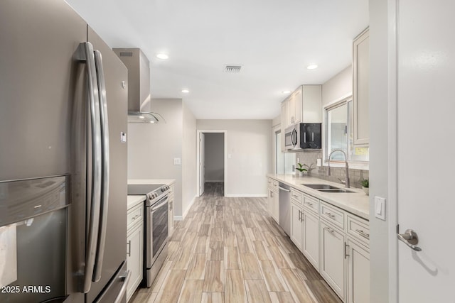 kitchen with sink, wall chimney range hood, appliances with stainless steel finishes, white cabinetry, and tasteful backsplash