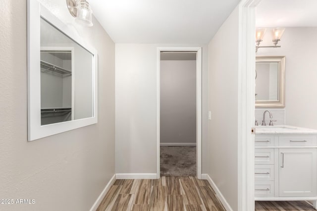 hallway featuring a sink, baseboards, and wood finished floors