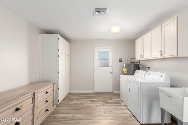 laundry area with water heater, separate washer and dryer, sink, cabinets, and light hardwood / wood-style flooring