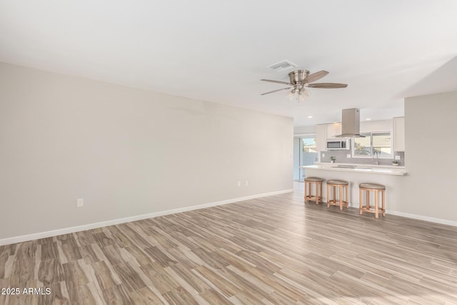 unfurnished living room featuring visible vents, light wood-style flooring, a ceiling fan, and baseboards