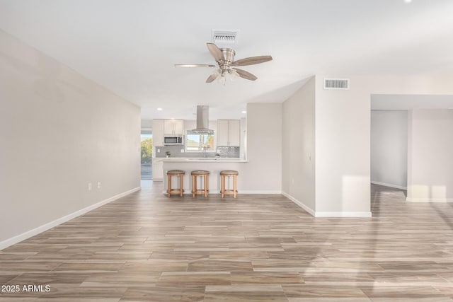 unfurnished living room featuring light wood-type flooring, visible vents, baseboards, and a ceiling fan