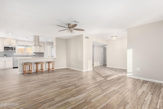 unfurnished living room featuring sink, ceiling fan, and light wood-type flooring