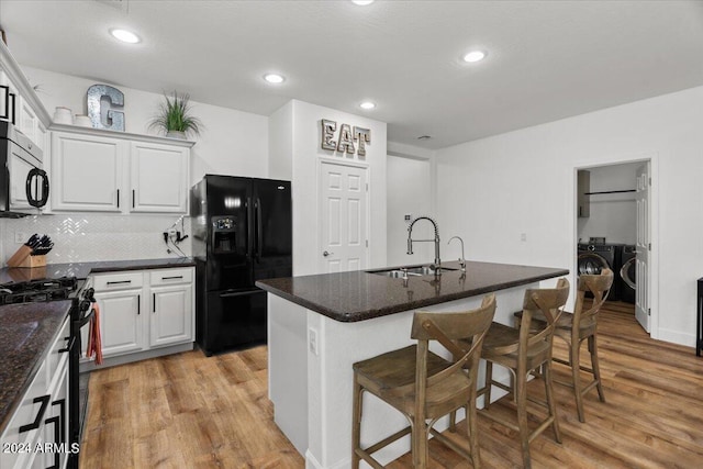 kitchen featuring an island with sink, white cabinetry, light wood-type flooring, black appliances, and sink