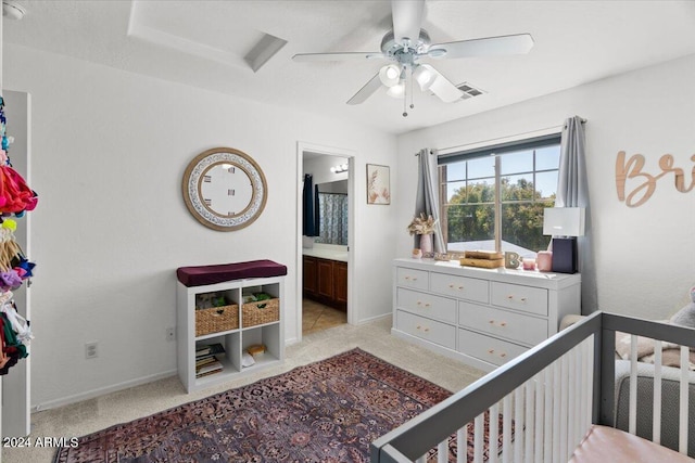 bedroom with connected bathroom, ceiling fan, light colored carpet, and a crib