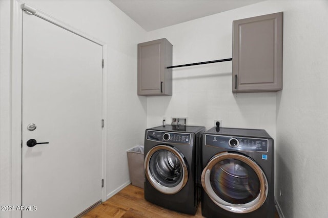 clothes washing area featuring cabinets, hardwood / wood-style flooring, and washing machine and dryer