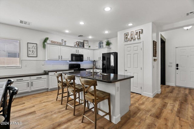 kitchen with light hardwood / wood-style floors, white cabinetry, black appliances, and a center island with sink