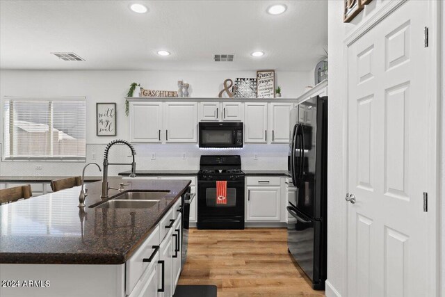 kitchen with black appliances, sink, white cabinetry, light hardwood / wood-style floors, and dark stone countertops